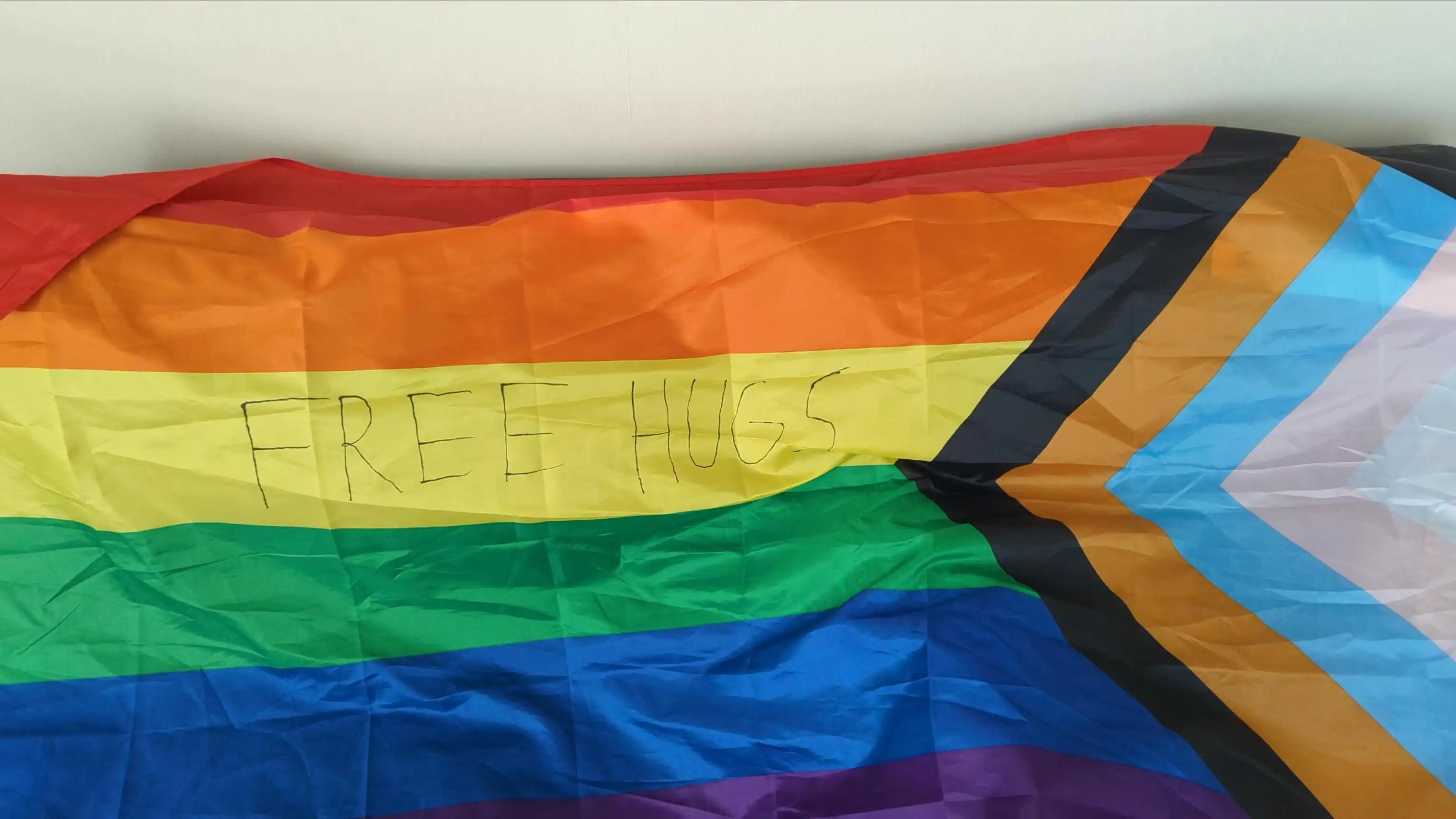 A progress flag with "FREE HUGS" written on in black on the yellow stripe