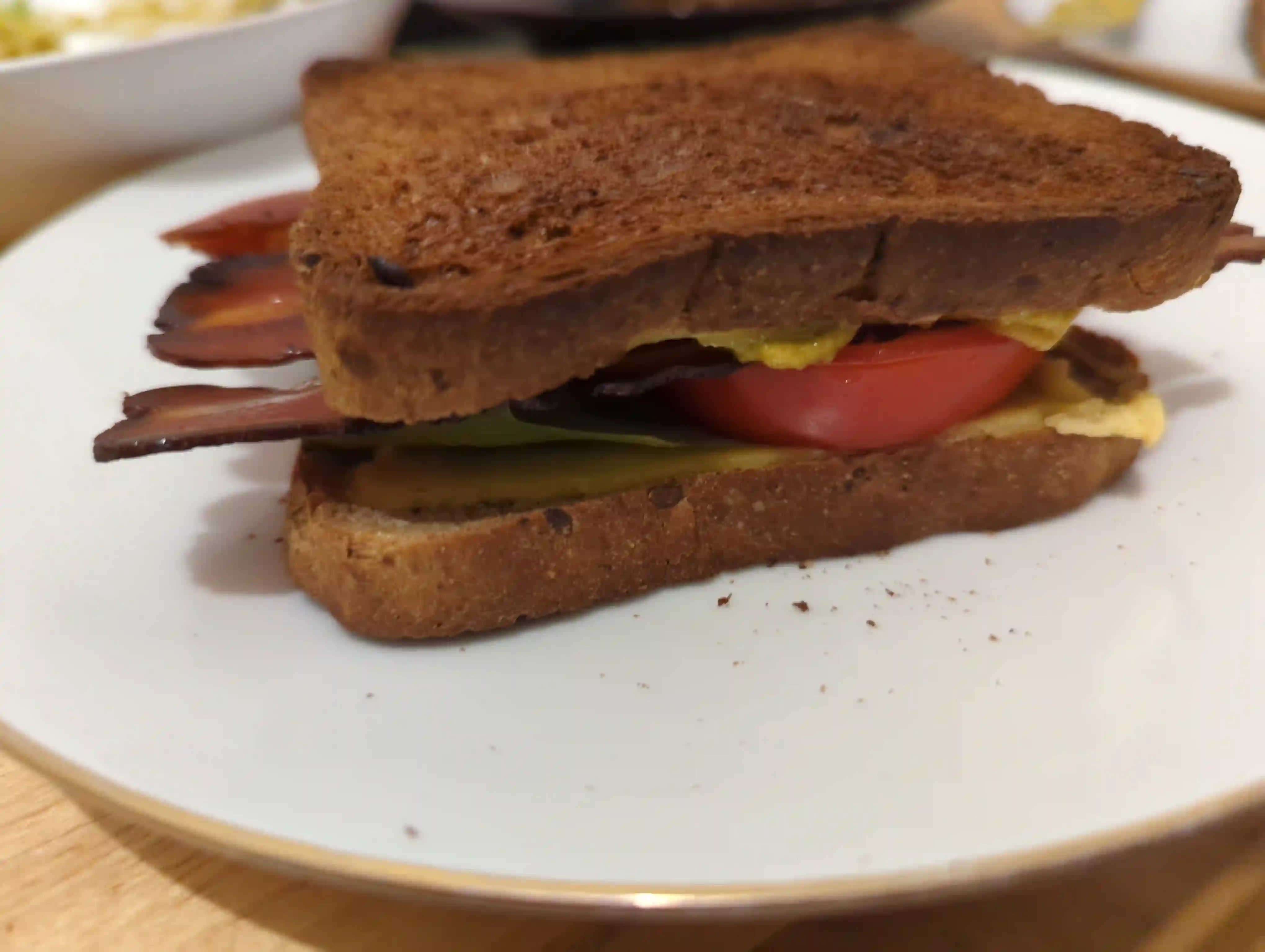 A sandwich w nicely toasted bread, crispy vegan bacon, guacamole, tomatoes, n a tiny bita lettuce
